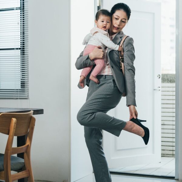 A mother holding her baby while removing her work shoe.
