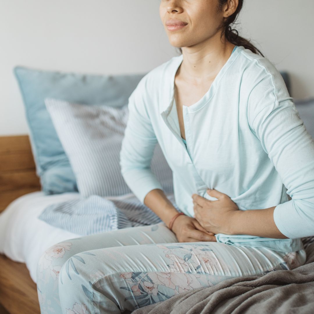 Woman with abdominal pain in bed using her hands to massage the area