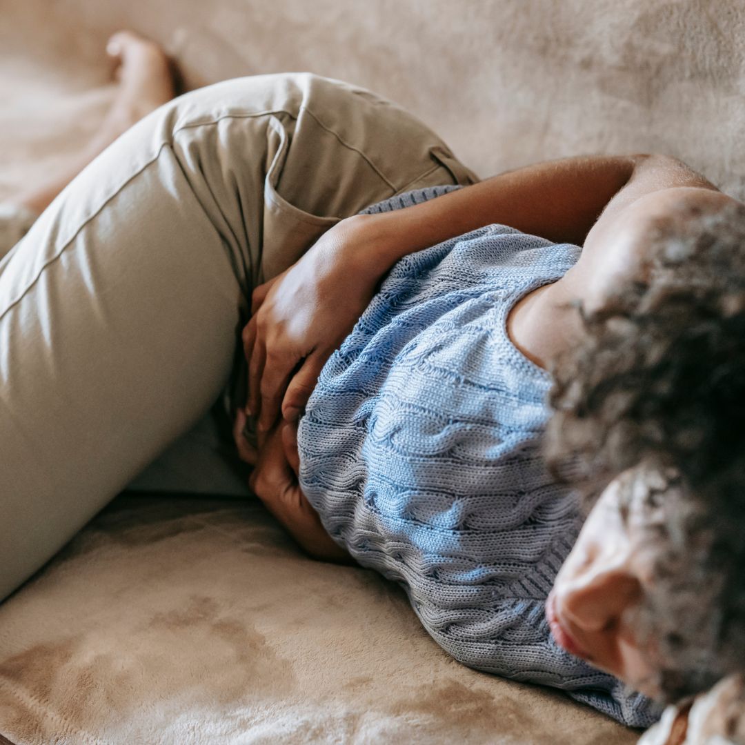 woman suffering from abdominal pain while laying on the couch